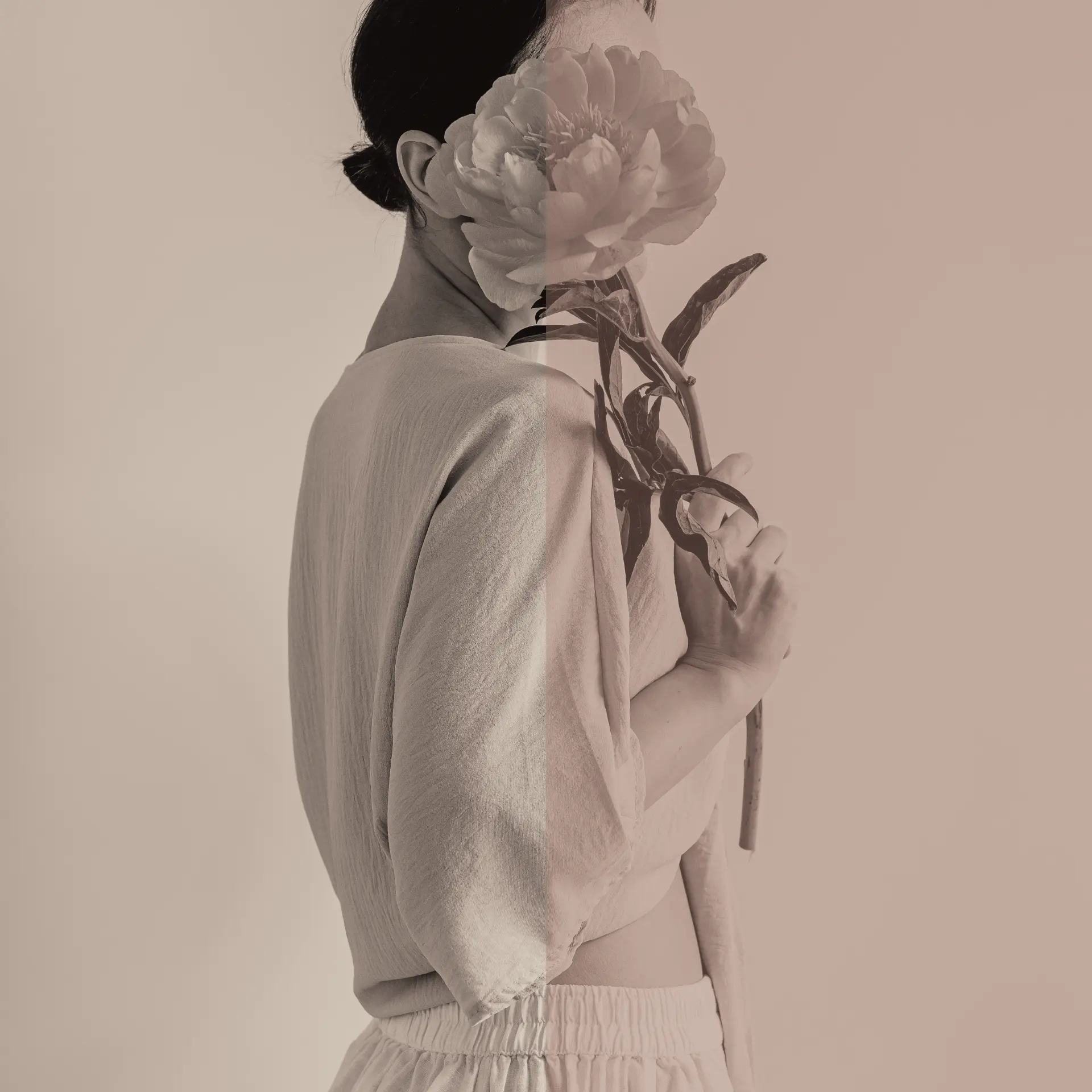 A woman seen from behind holding a peony over her shoulder